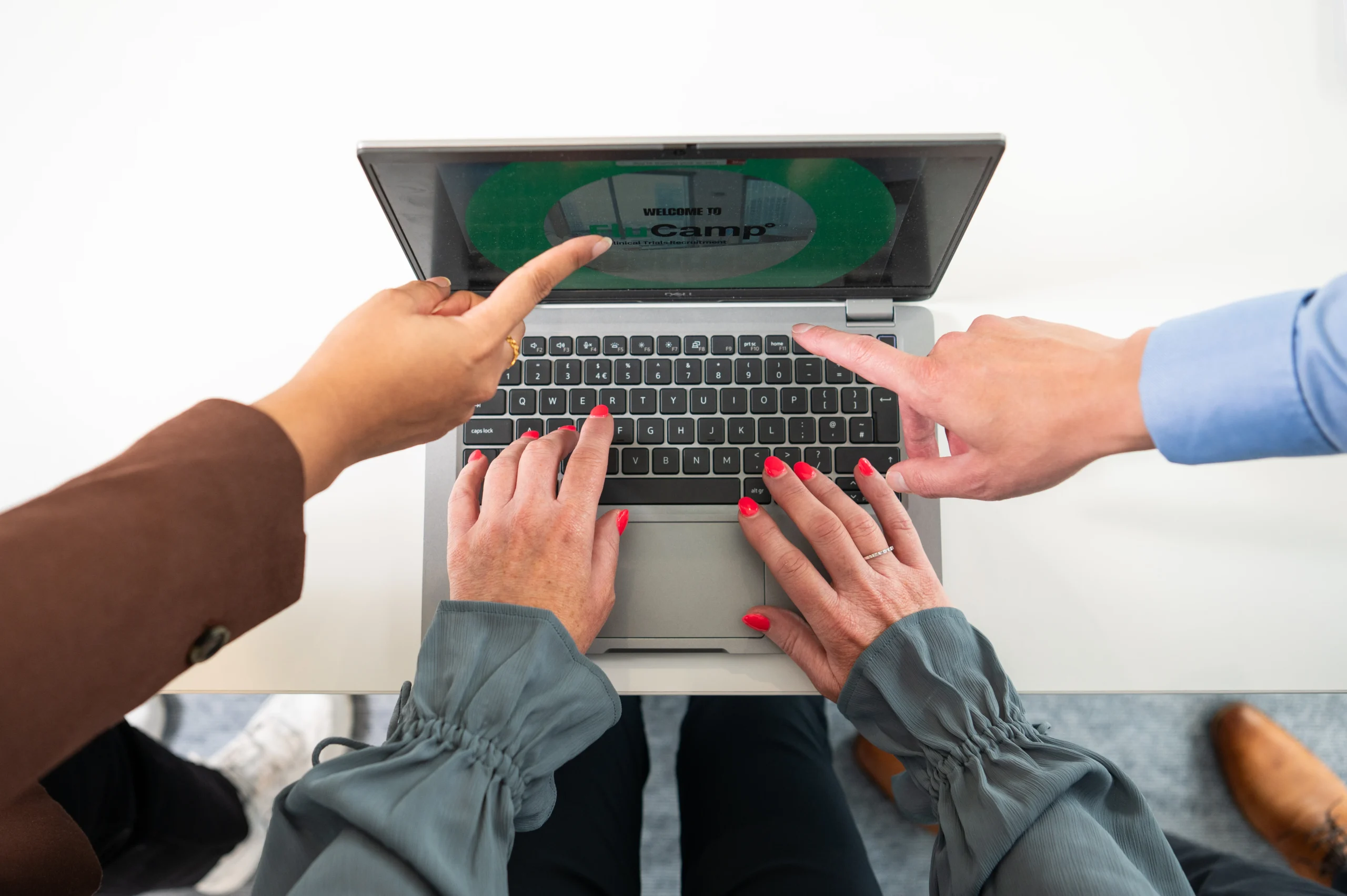 Hands pointing at a laptop screen showing the FluCamp Clinical Trial Recruitment logo